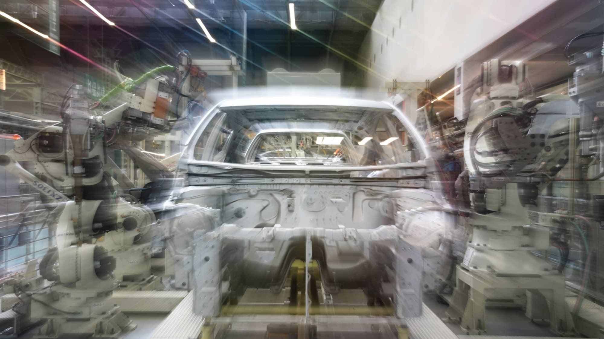 A car assembly line: robotic arms working over a body shell in motion.