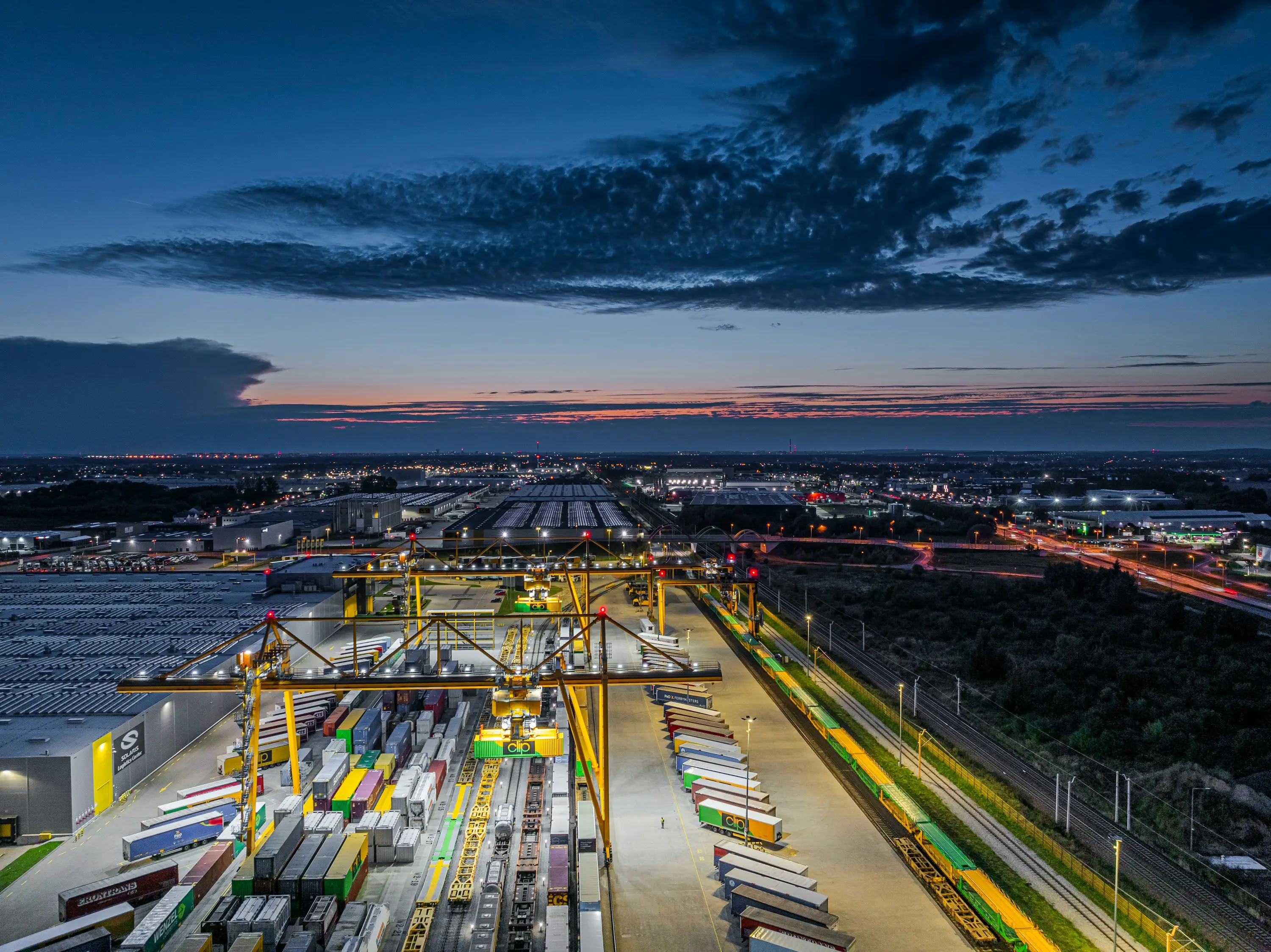 A container terminal at dusk, with gantry cranes and stacked containers.