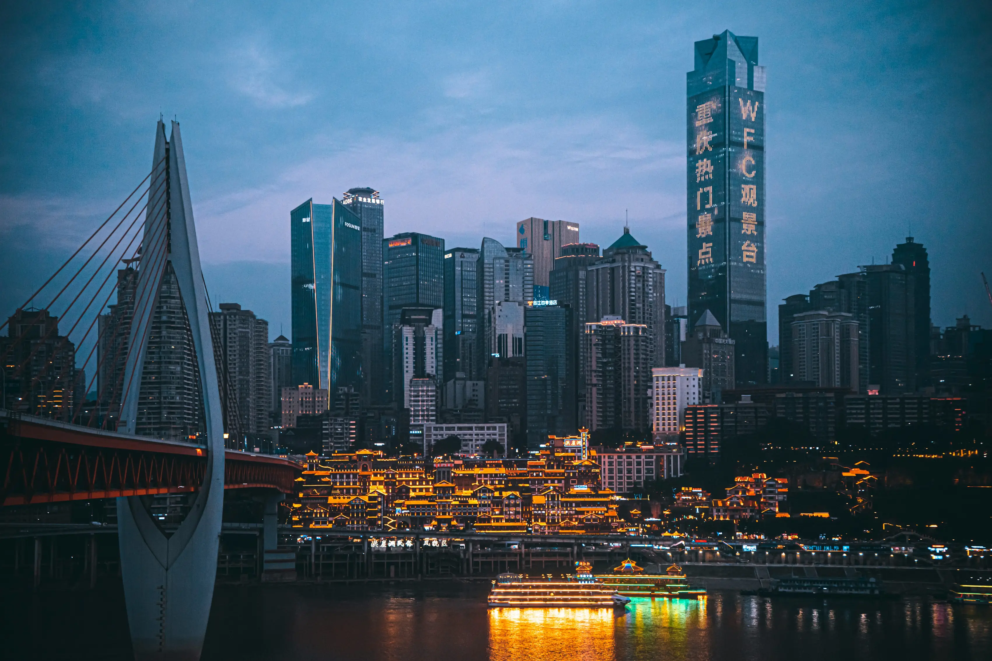A city's financial district at night, with a cable-stayed bridge in the foreground.
