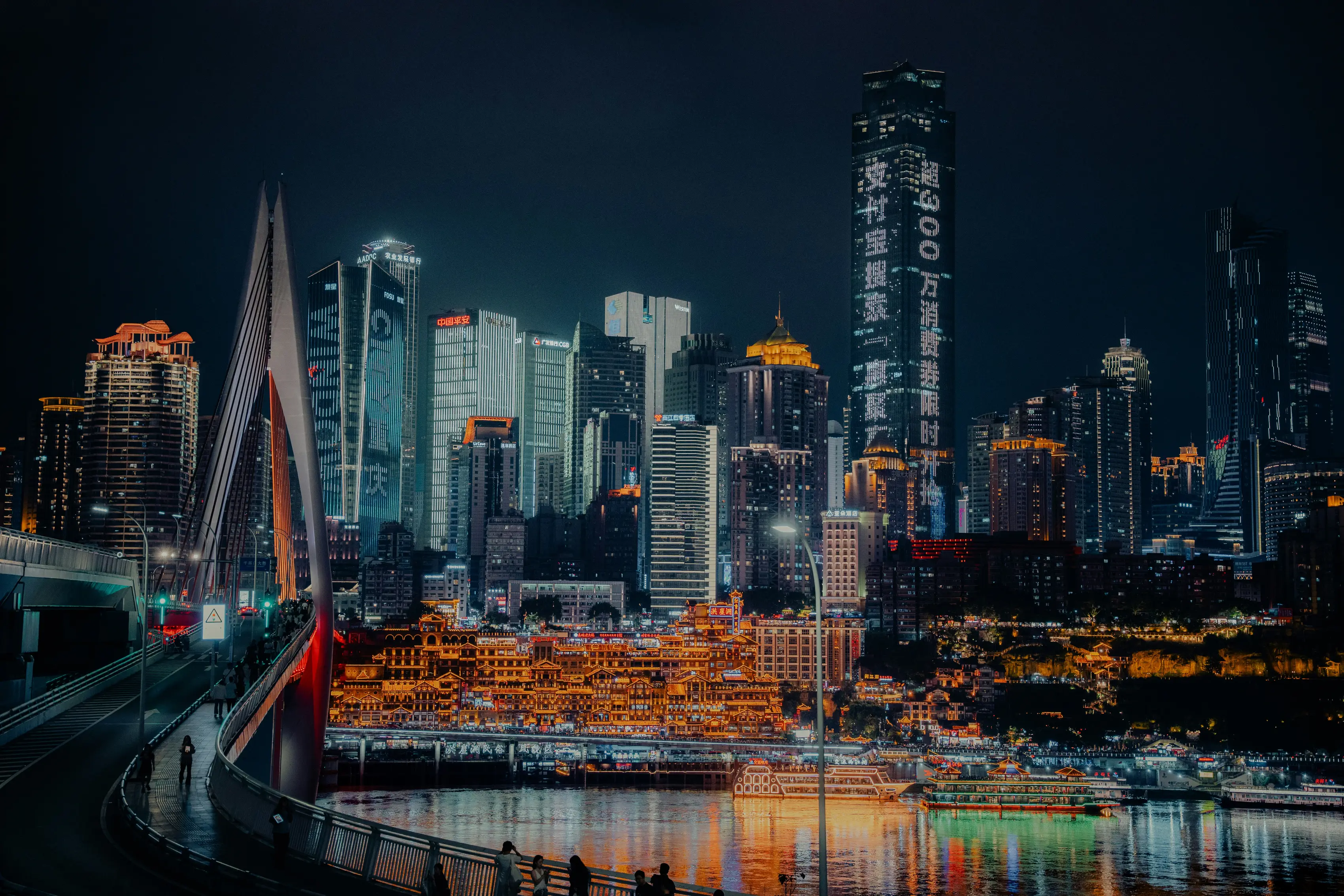 A city skyline at night, its lit towers reflected in the river.