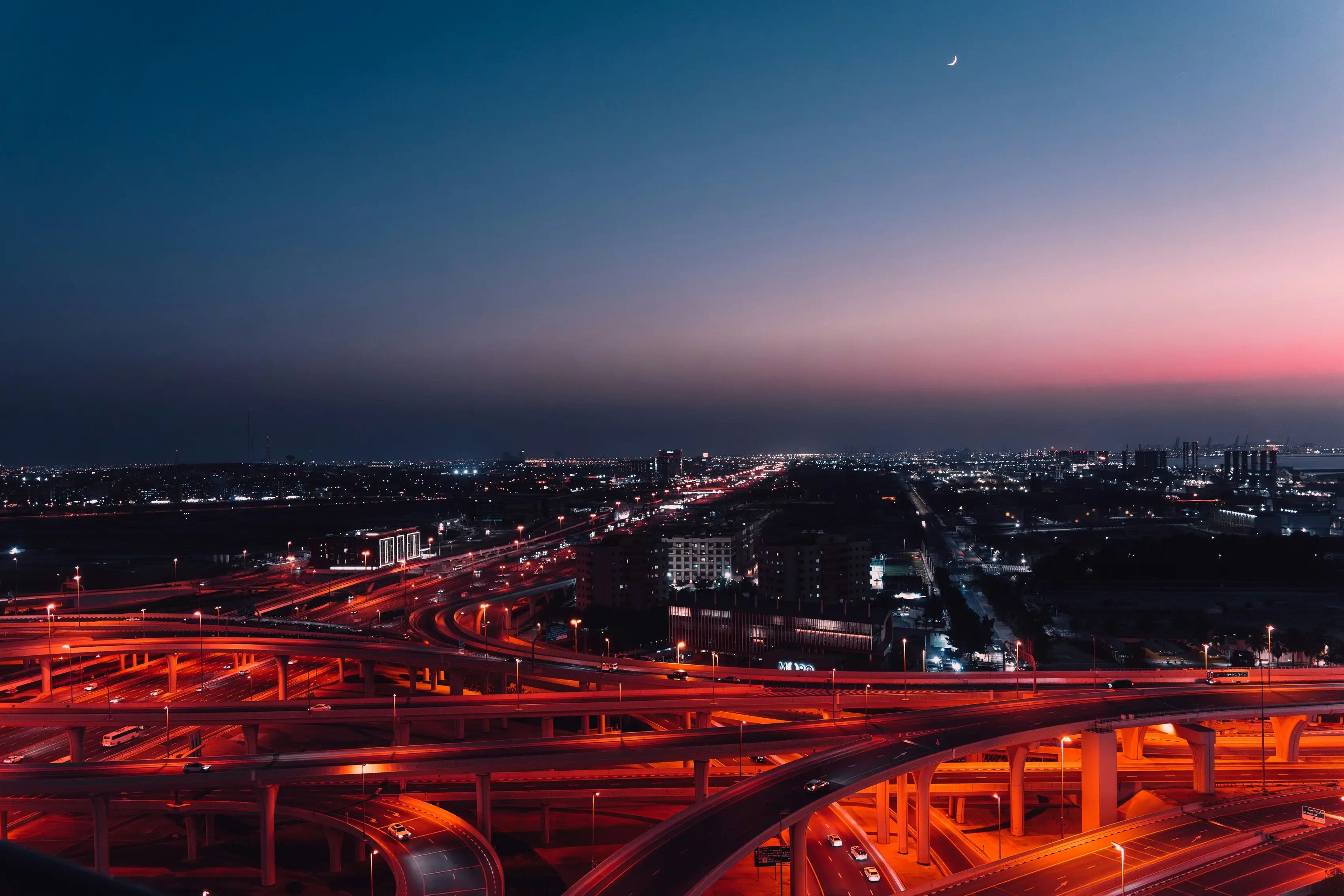 A motorway interchange from the air at dusk, with the red trails of traffic.