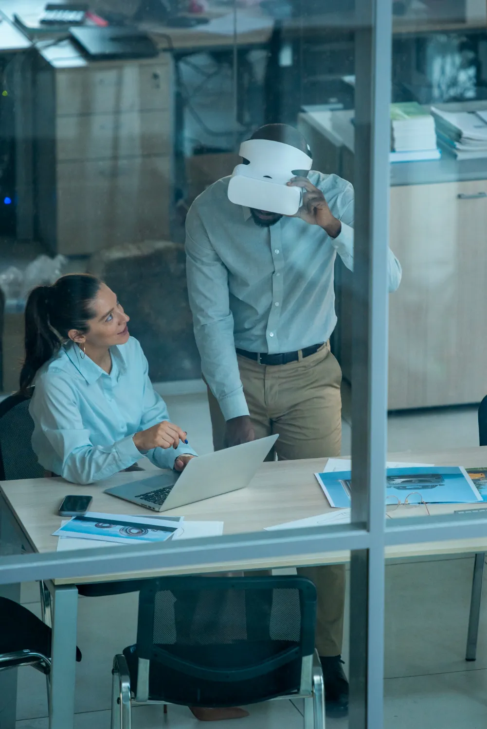 Dos personas prueban un visor en una oficina, vistas a través de un cristal